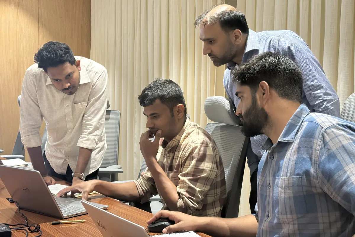 A mentor leaning over a laptop, working through code with three interns